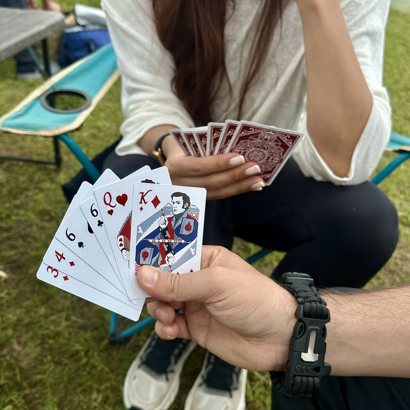 Two players holding hands of Fragments cards outdoors, one hand showing the king of diamonds
